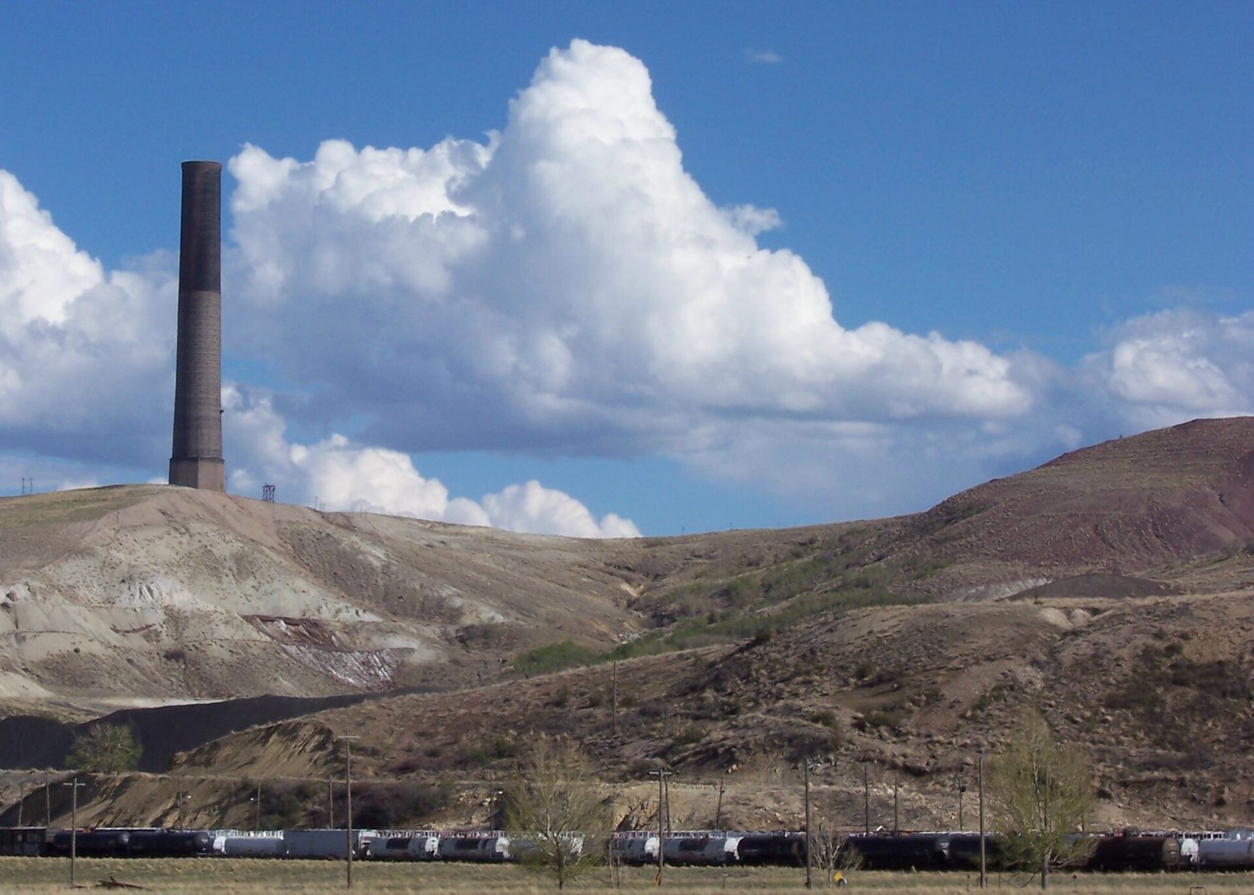 The dark brick stack on a bare hill under a big white cloud, a freight train passing below